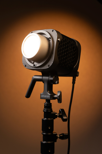 Amaran Halo 300x bi-color COB LED light mounted on a studio stand with a glowing warm-tone background